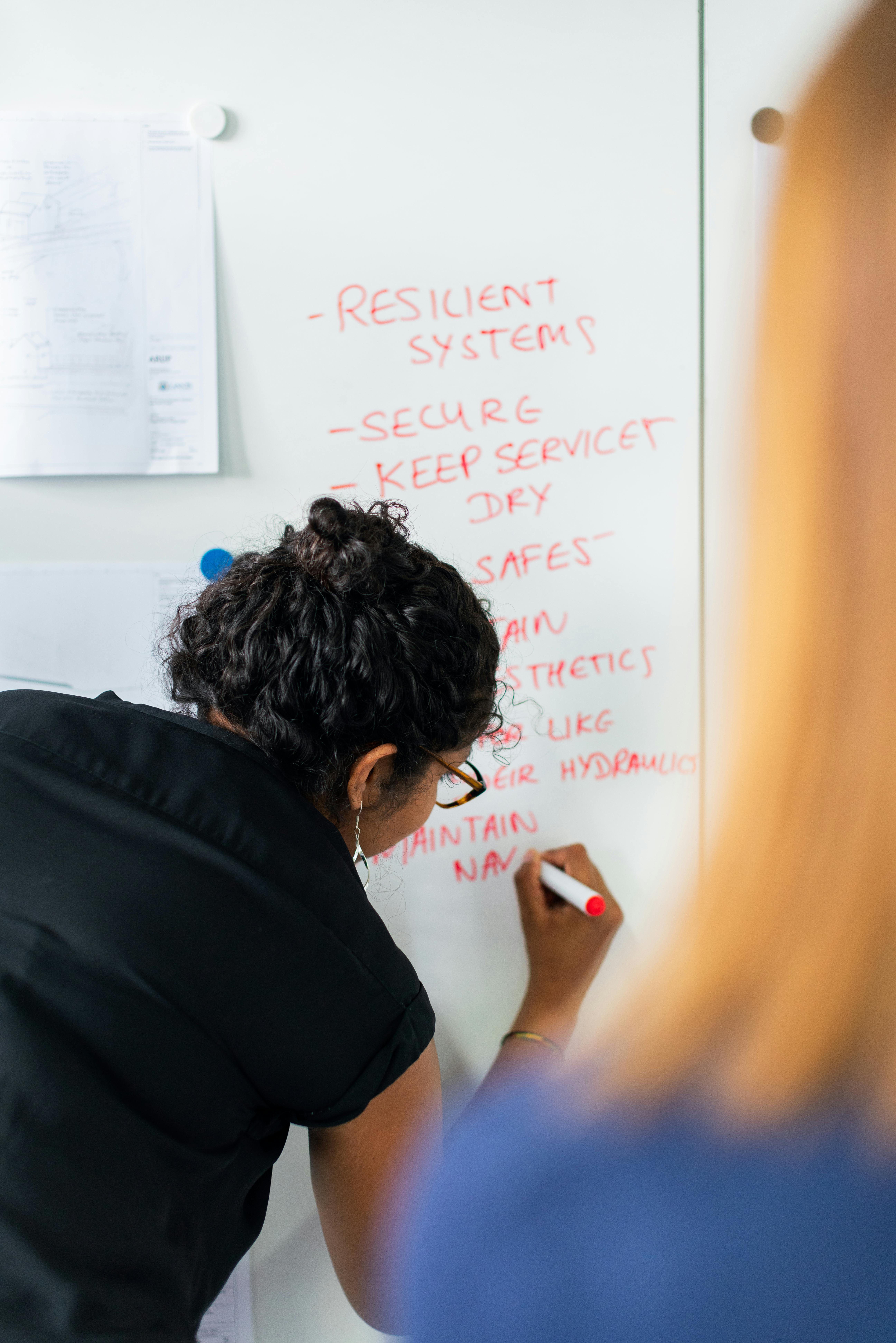 Engineer writing notes on a whiteboard with a red marker